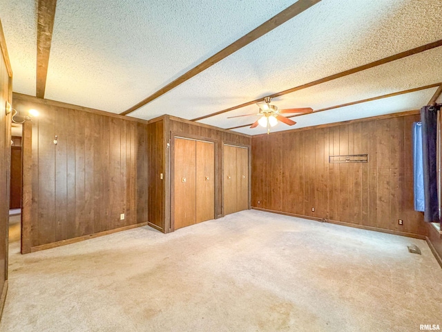 interior space with light colored carpet, wood walls, ceiling fan, and a textured ceiling