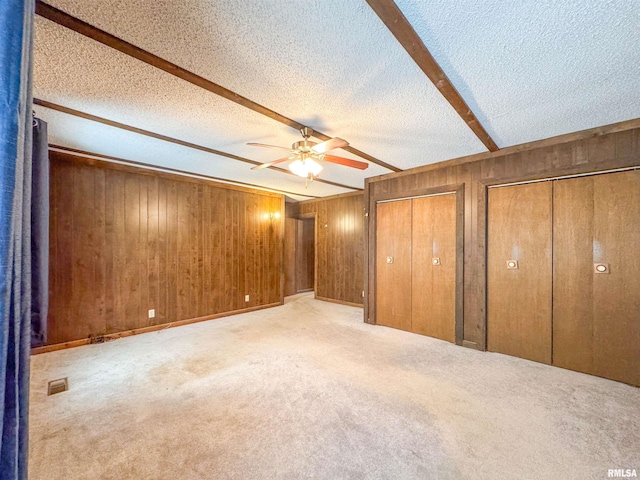 unfurnished bedroom featuring a textured ceiling, multiple closets, wood walls, ceiling fan, and light carpet