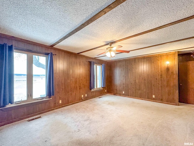 carpeted spare room featuring wooden walls, a textured ceiling, ceiling fan, and beam ceiling