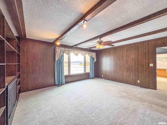 spare room with beam ceiling, light carpet, wood walls, and a textured ceiling