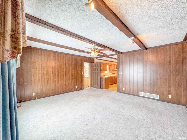 unfurnished living room featuring beam ceiling, light colored carpet, wood walls, and a textured ceiling