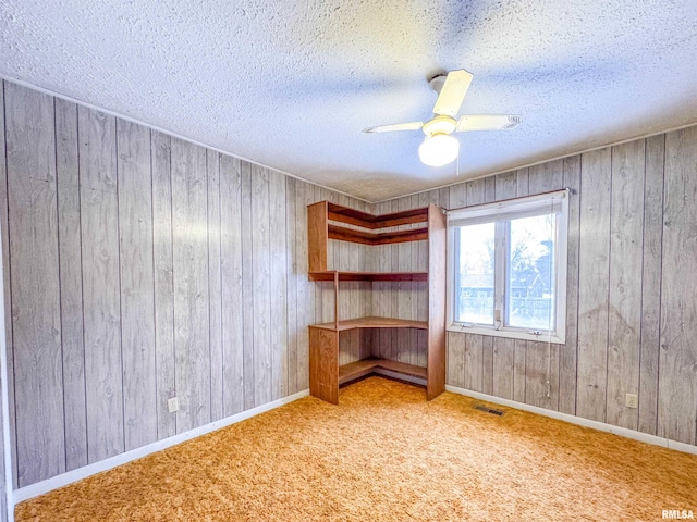 carpeted empty room featuring a textured ceiling, ceiling fan, and wooden walls