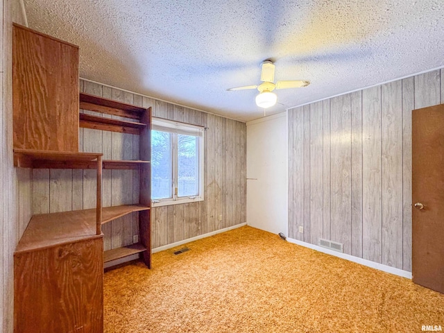 unfurnished room featuring light colored carpet, wood walls, and ceiling fan