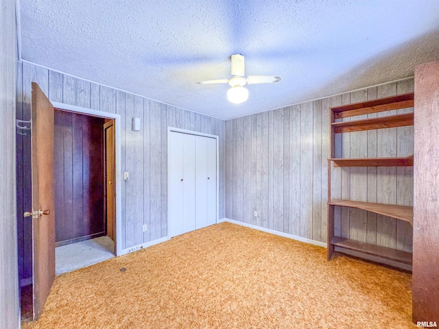 unfurnished bedroom featuring wooden walls, carpet floors, ceiling fan, and a textured ceiling