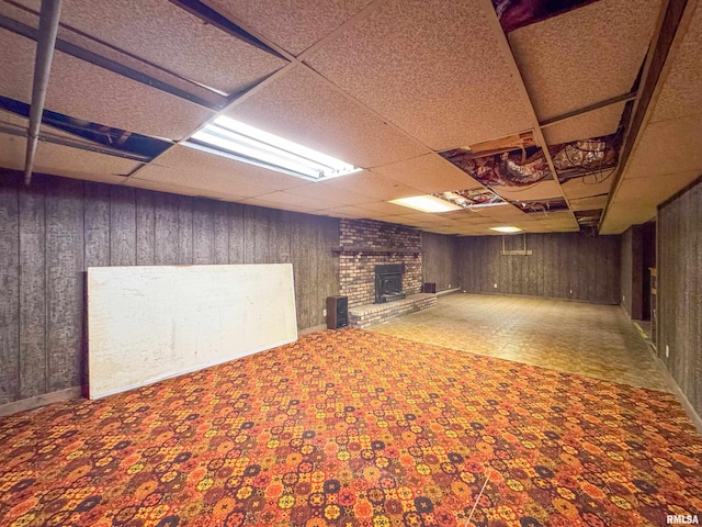 basement featuring a fireplace, wood walls, and a paneled ceiling