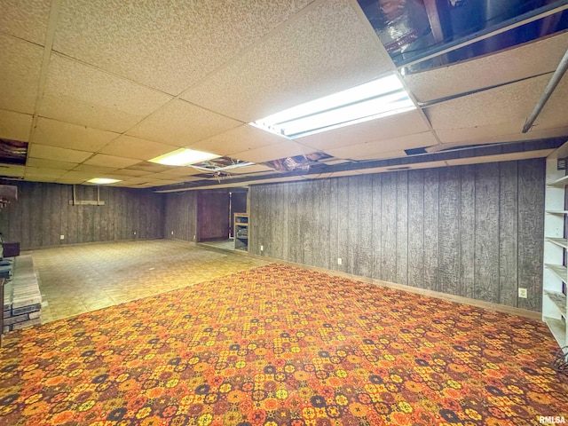 basement with a paneled ceiling, wooden walls, and carpet flooring