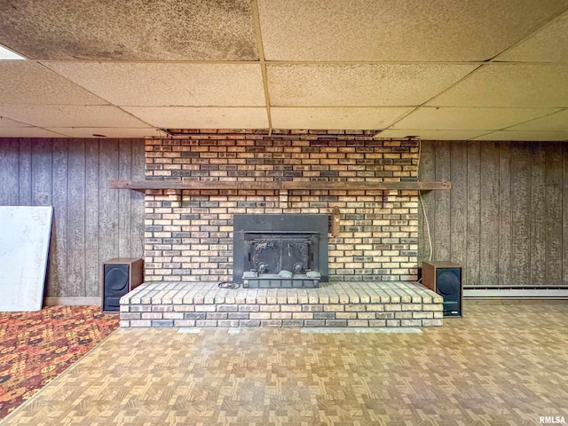 unfurnished living room with a baseboard radiator, parquet flooring, wood walls, and a drop ceiling