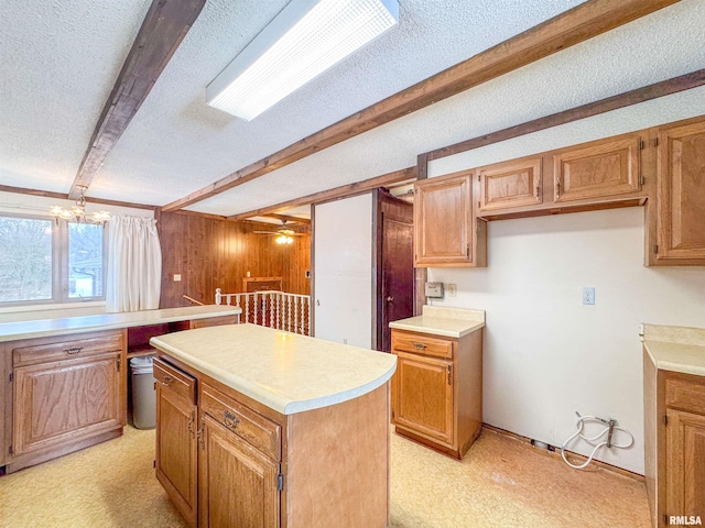 kitchen featuring a textured ceiling, wooden walls, a kitchen island, beam ceiling, and ceiling fan with notable chandelier