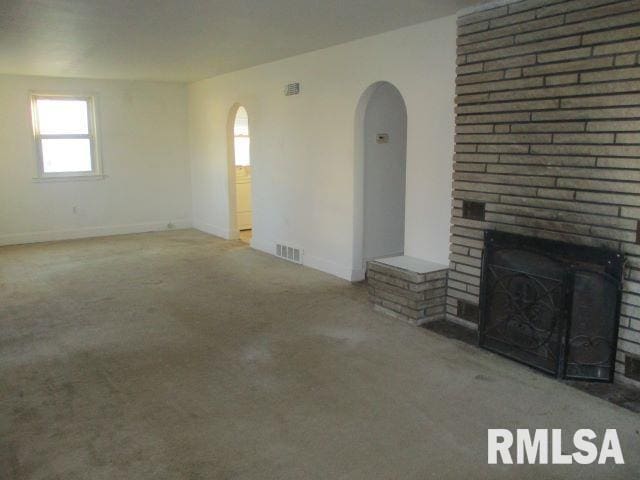 unfurnished living room with a brick fireplace and carpet flooring