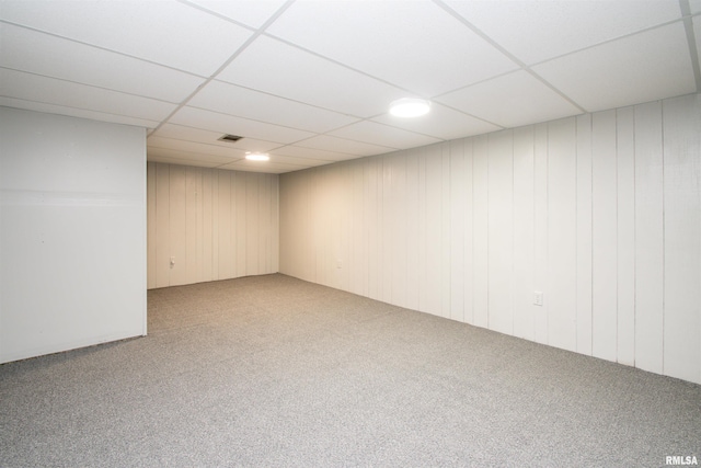 basement with carpet, wood walls, and a drop ceiling