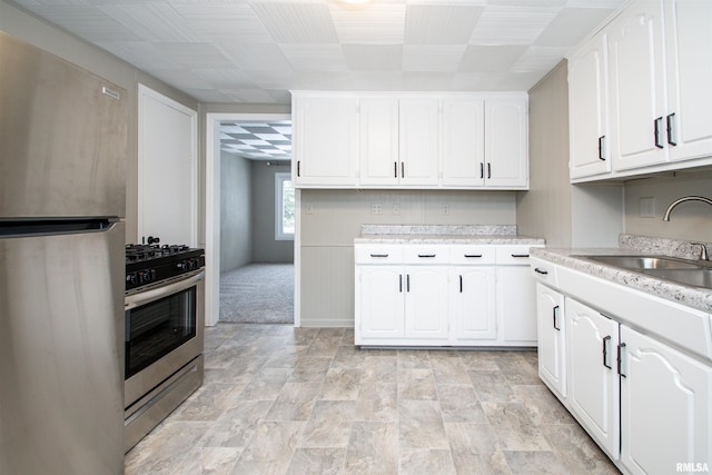 kitchen featuring sink, light colored carpet, appliances with stainless steel finishes, and white cabinetry