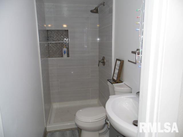 bathroom with sink, tiled shower, and toilet