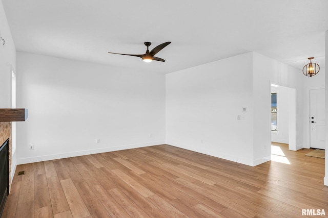 unfurnished living room with a tiled fireplace, ceiling fan with notable chandelier, and light hardwood / wood-style flooring