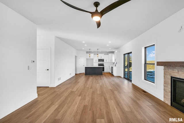 unfurnished living room featuring ceiling fan, light wood-type flooring, sink, and a fireplace