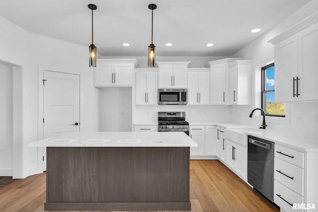 kitchen with stainless steel appliances, a center island, light hardwood / wood-style floors, white cabinets, and decorative light fixtures