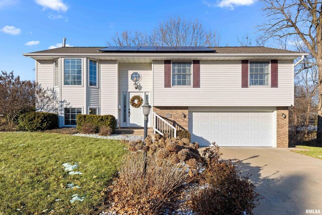 bi-level home featuring a garage, a front lawn, and solar panels