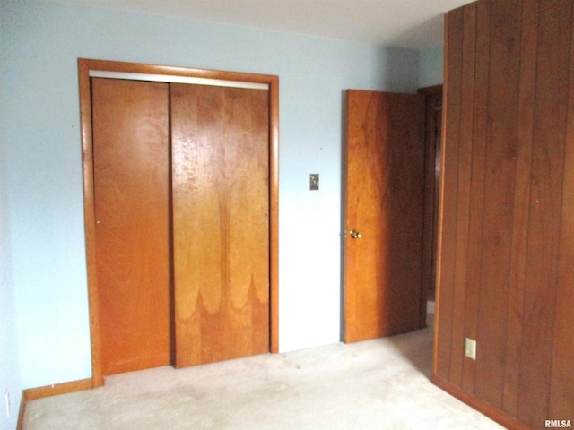 unfurnished bedroom featuring light carpet, a closet, and wood walls