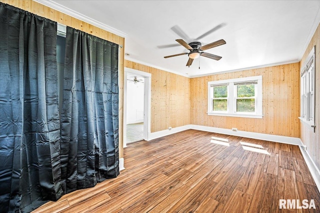 spare room with ceiling fan, wood-type flooring, wooden walls, and ornamental molding