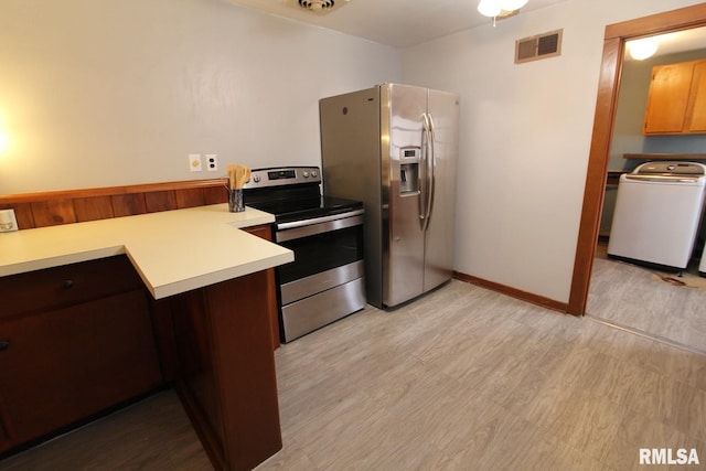 kitchen with light wood-type flooring, appliances with stainless steel finishes, dark brown cabinetry, and washer / dryer