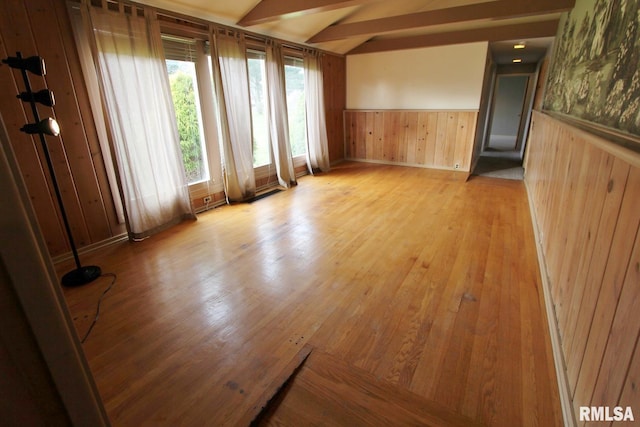 spare room featuring lofted ceiling, wood walls, and light wood-type flooring