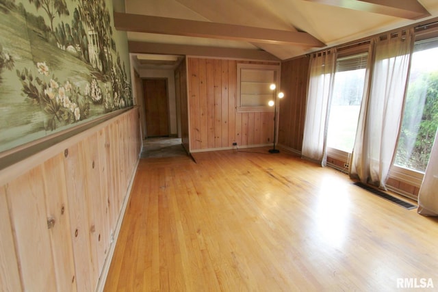 spare room with wood walls, light hardwood / wood-style flooring, and vaulted ceiling with beams