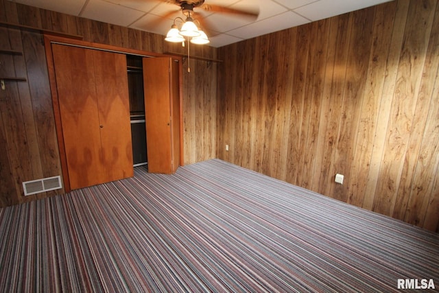 unfurnished bedroom featuring a closet, ceiling fan, wood walls, and carpet flooring