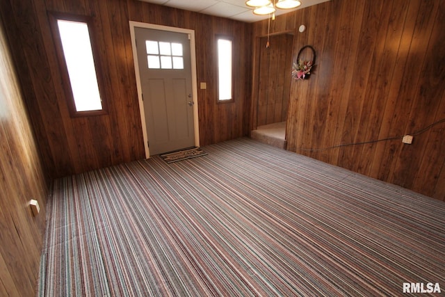 carpeted foyer entrance featuring wooden walls