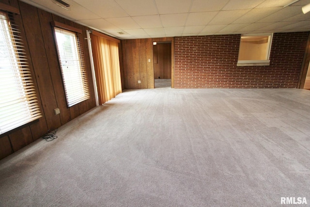 basement featuring wood walls, carpet flooring, brick wall, and a drop ceiling