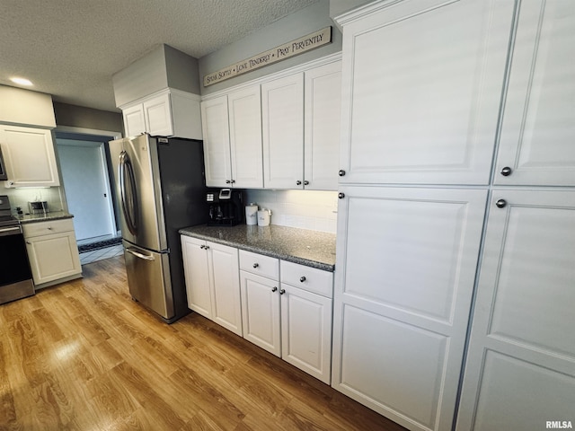 kitchen featuring a textured ceiling, white cabinetry, stainless steel appliances, light hardwood / wood-style floors, and backsplash