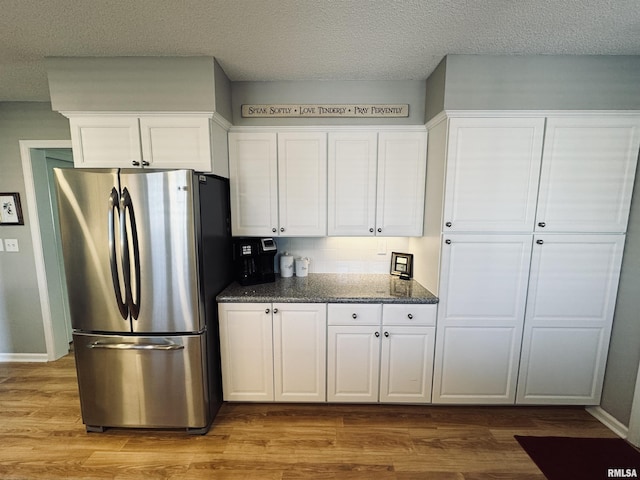 kitchen featuring white cabinets, light wood-type flooring, dark stone counters, and stainless steel refrigerator