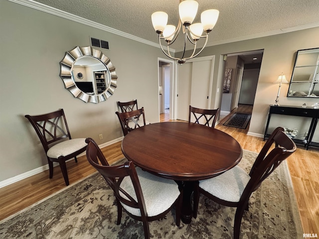 dining area featuring light wood-type flooring, ornamental molding, a chandelier, and a textured ceiling