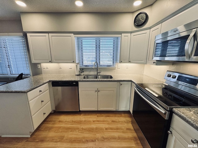 kitchen featuring appliances with stainless steel finishes, white cabinetry, decorative backsplash, sink, and light wood-type flooring