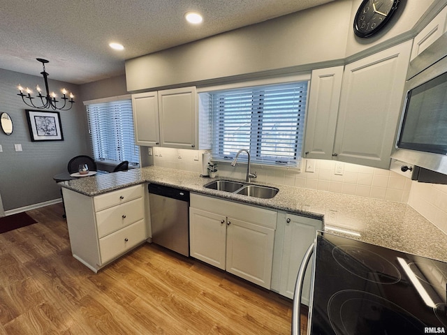 kitchen featuring kitchen peninsula, appliances with stainless steel finishes, a notable chandelier, white cabinets, and sink