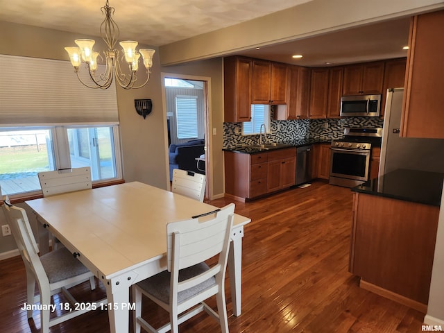 kitchen with dark wood-type flooring, appliances with stainless steel finishes, hanging light fixtures, decorative backsplash, and a chandelier