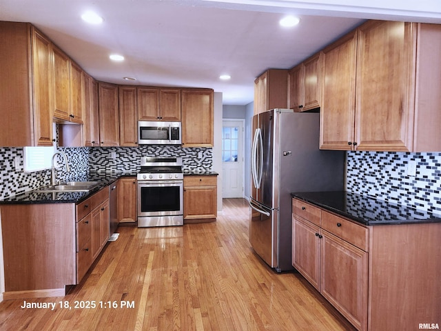 kitchen with dark stone countertops, appliances with stainless steel finishes, sink, and light wood-type flooring