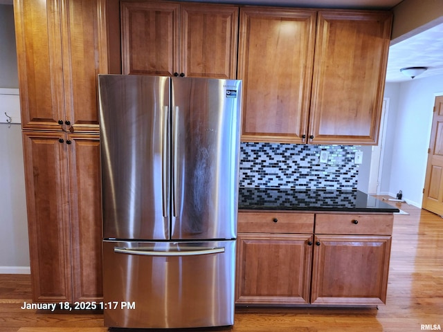 kitchen featuring stainless steel fridge, light wood-type flooring, decorative backsplash, and dark stone countertops