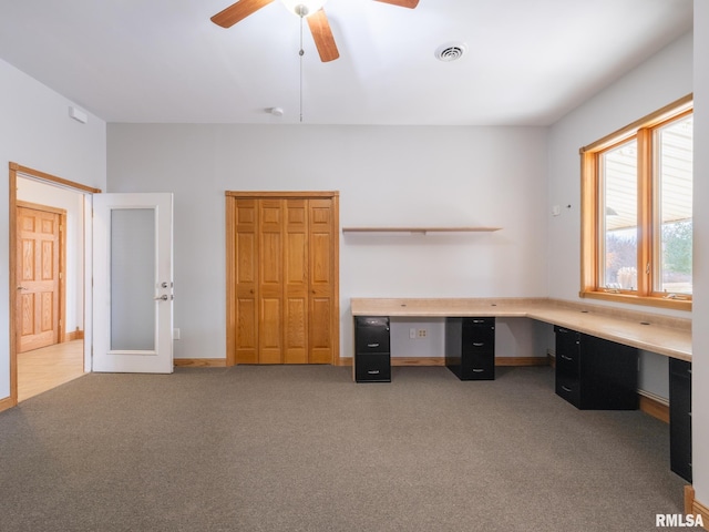 unfurnished office with ceiling fan, built in desk, and carpet flooring