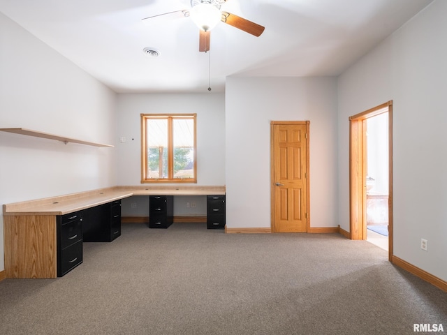 unfurnished office featuring built in desk, light carpet, and ceiling fan