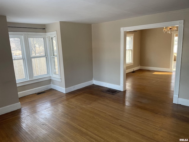 unfurnished room featuring an inviting chandelier, a healthy amount of sunlight, and dark hardwood / wood-style floors