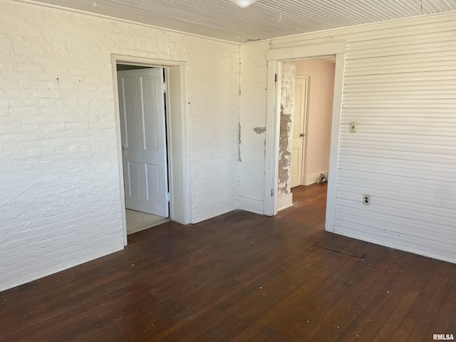 spare room with brick wall and dark hardwood / wood-style flooring