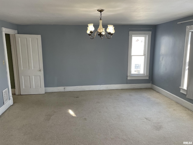 carpeted empty room featuring a notable chandelier