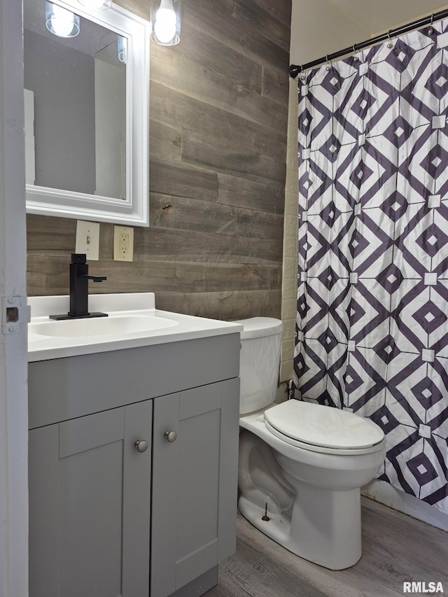 bathroom with toilet, wooden walls, hardwood / wood-style flooring, and vanity