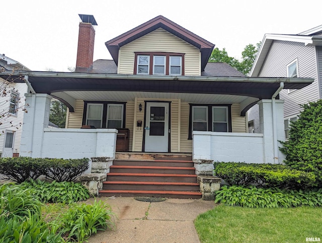 bungalow with a porch, concrete block siding, a shingled roof, and a chimney