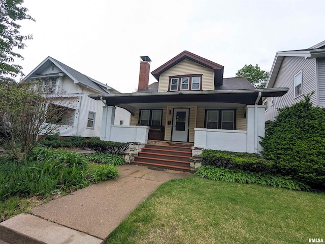 bungalow-style home featuring a porch, concrete block siding, a chimney, and a front lawn