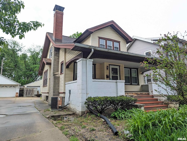 view of front facade with a porch, cooling unit, a garage, an outdoor structure, and a chimney