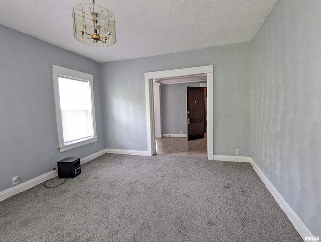 carpeted spare room featuring a textured ceiling and a chandelier