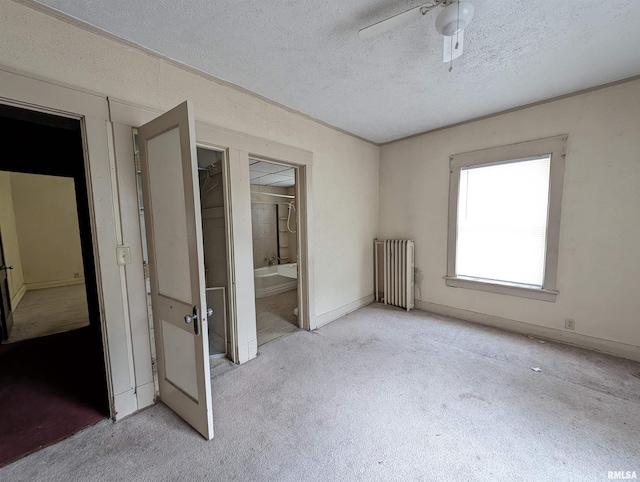 unfurnished bedroom featuring a textured ceiling, radiator heating unit, ensuite bath, ceiling fan, and light colored carpet