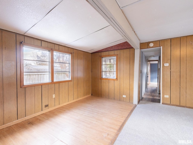 unfurnished room with wood walls, plenty of natural light, and lofted ceiling