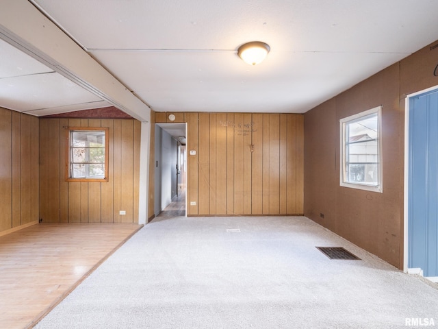 carpeted empty room with vaulted ceiling, plenty of natural light, and wooden walls