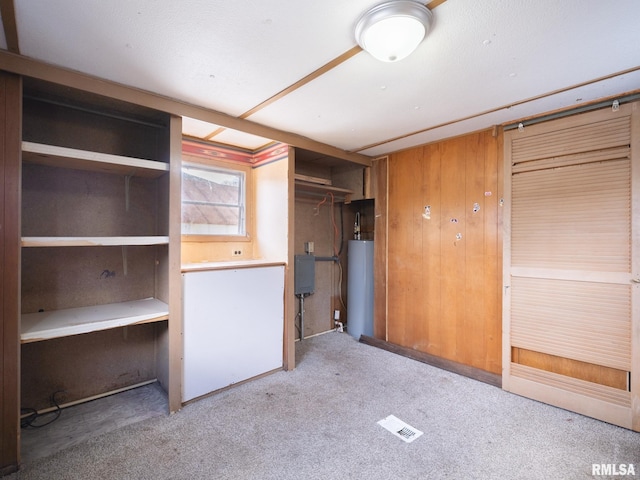 unfurnished bedroom featuring light carpet, a closet, wood walls, and gas water heater